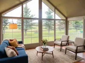 Interior of a 3-season vinyl sunroom with large screened windows, seating, and a peaceful lakefront yard view.