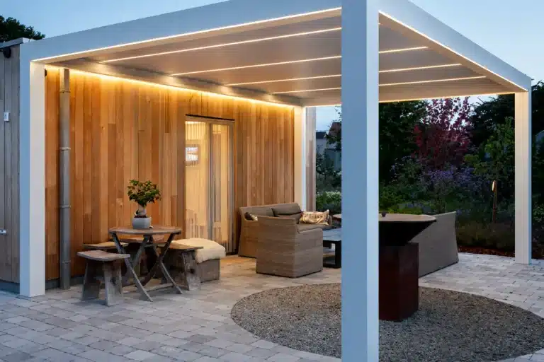 White attached louvered pergola with built-in LED lighting over a furnished patio