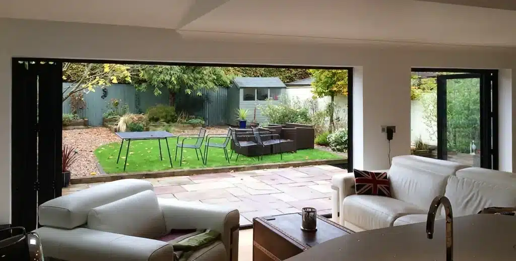 Open bi-fold doors connect a living room to a garden patio with outdoor seating.