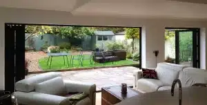 Open bi-fold doors connect a living room to a garden patio with outdoor seating.