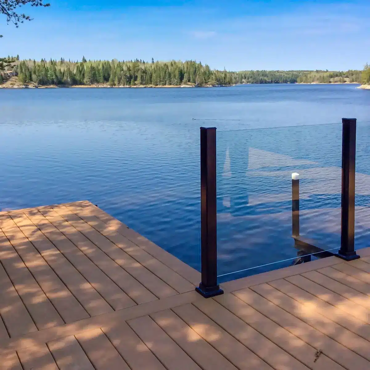 Clear topless glass railing with black aluminum posts overlooking a lake