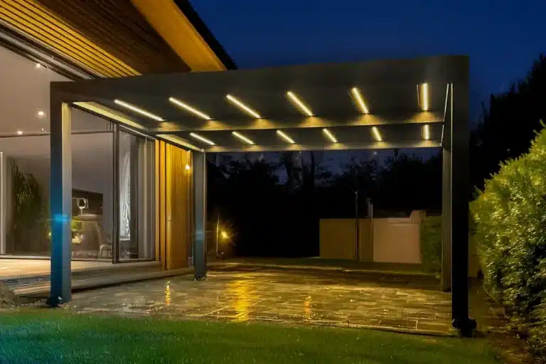 Attached black louvered pergola with LED-lit roof sheltering a wet patio at night