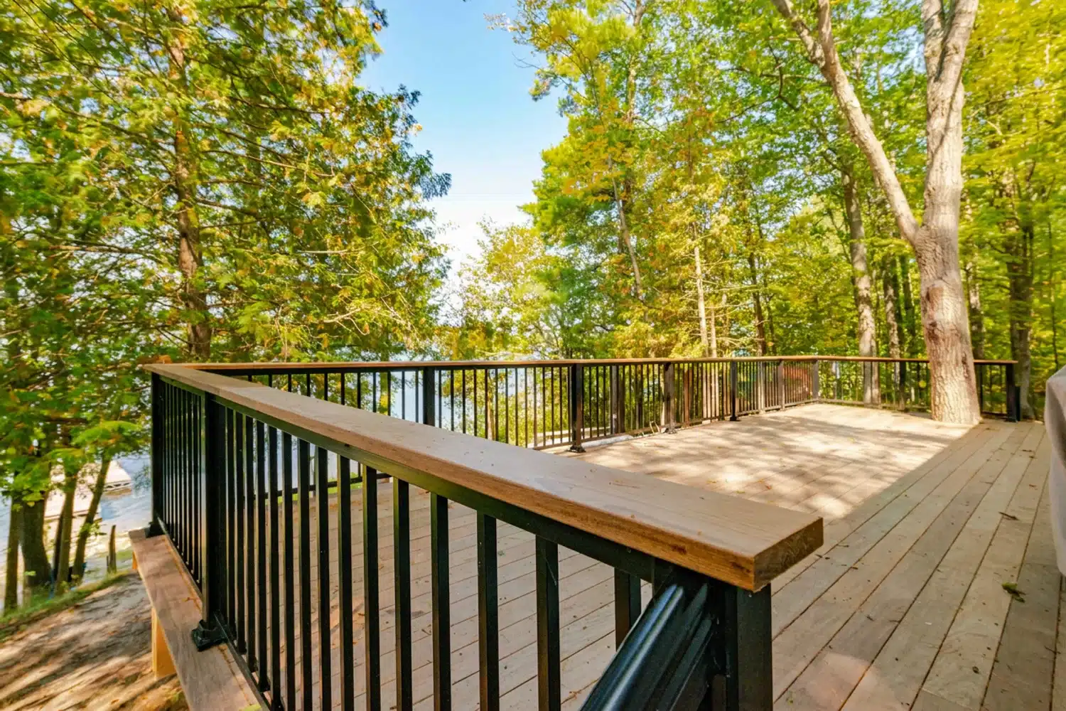 Black aluminum picket railing around a wooded lake deck with water visible through the trees