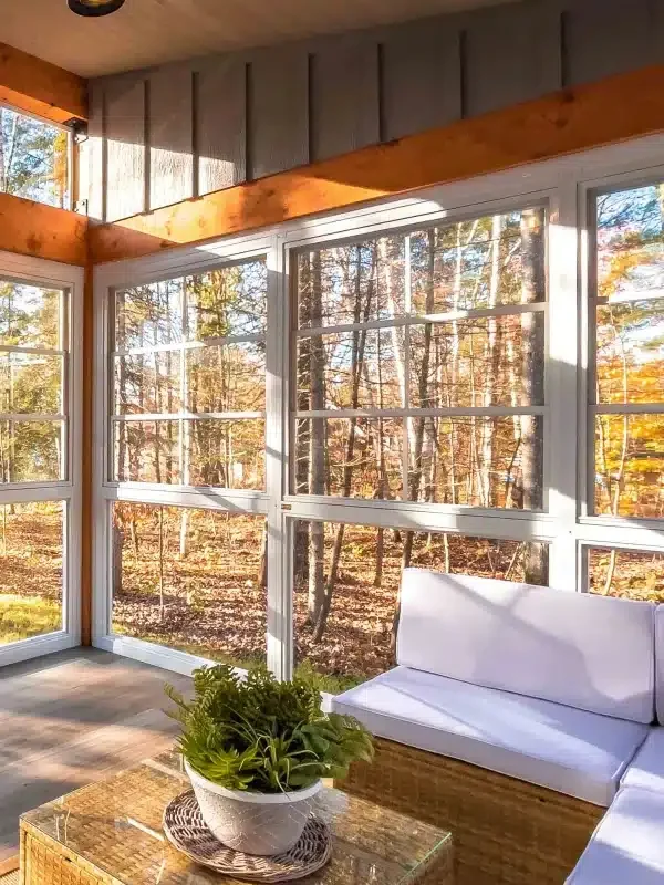 White-framed enclosed porch with seating overlooking autumn trees