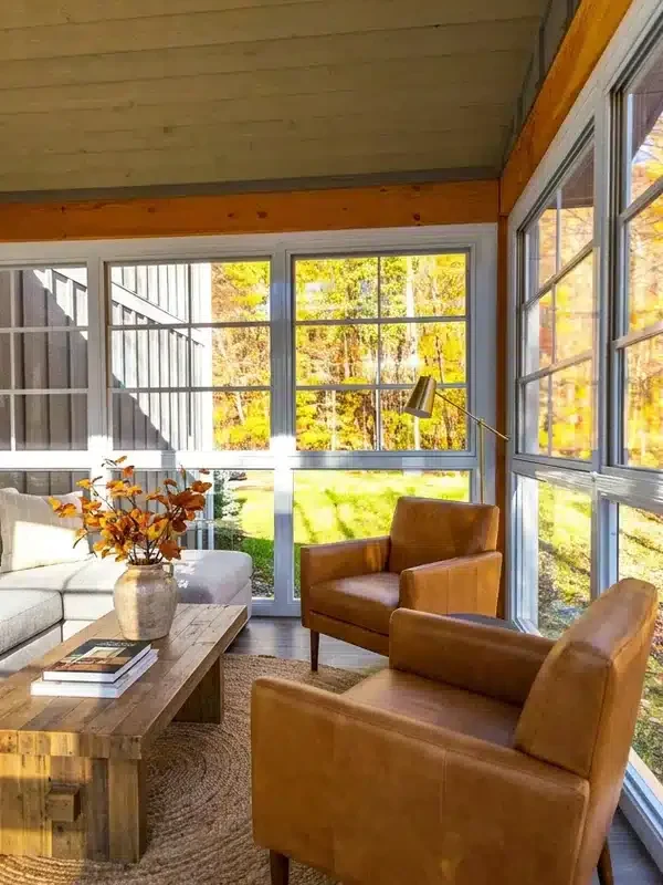 Cozy sunroom reading nook with leather chairs and golden autumn foliage