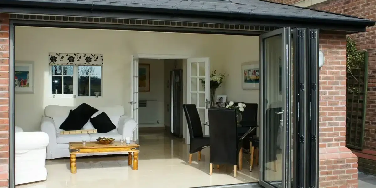 Folding glass wall stacked open beside a living and dining room leading to a patio.